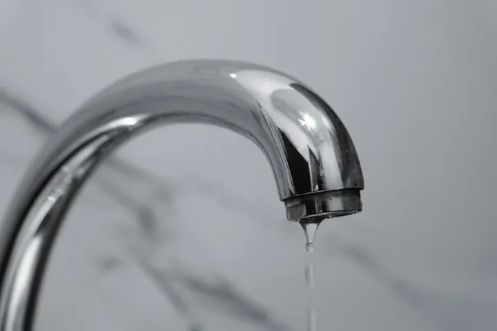 Из носика хромированного смесителя капает вода